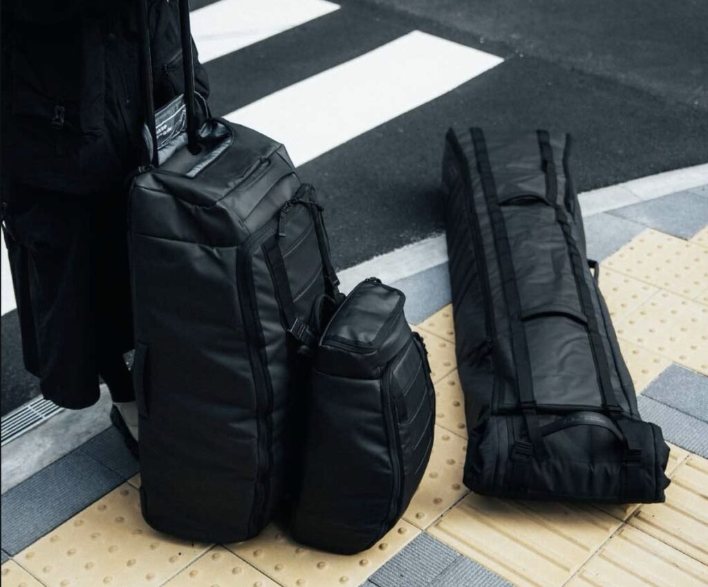 Black Db Journey travel luggage set on a crosswalk, including a roller bag, a smaller pack, and a long snow gear bag.